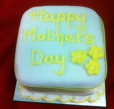 A square Mother's Day cake with pale icing and piped yellow flowers